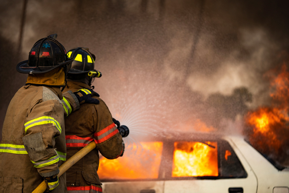 Bil som brinner och två brandmän hjälps åt för att släcka branden.